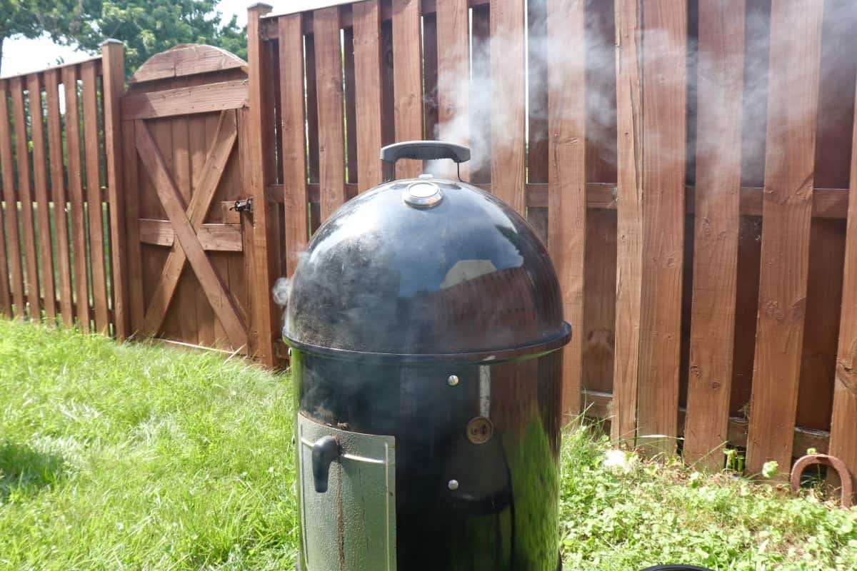 Thick white smoke coming out the top vent of a Weber Smokey Mountain smok.