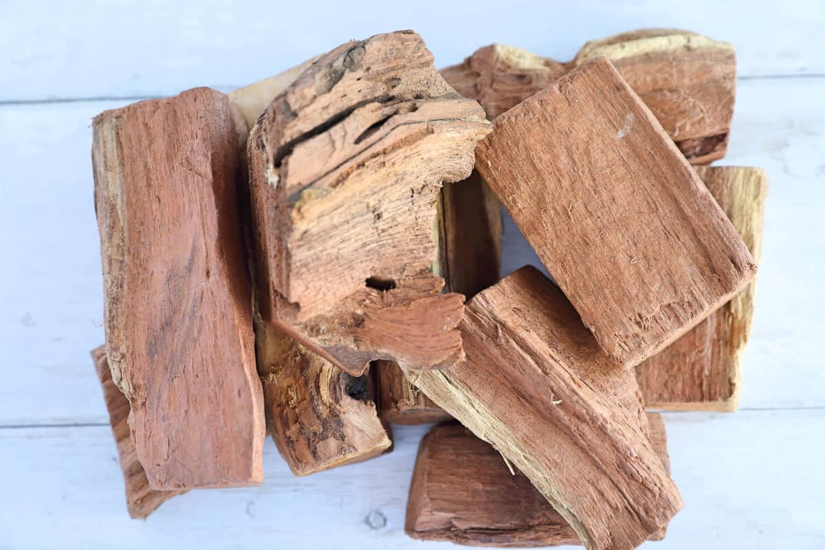 A pile of mesquite smoking wood chunks on a white wooden table.
