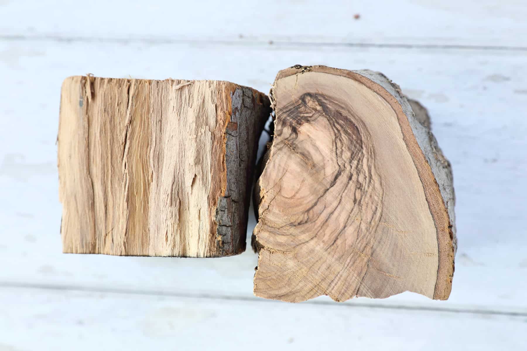 Two chunks of olive wood on a white wooden table.