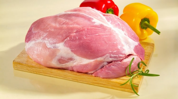 raw, boneless, pork cushion meat, on a cutting board with a red and yellow pepper in the background
