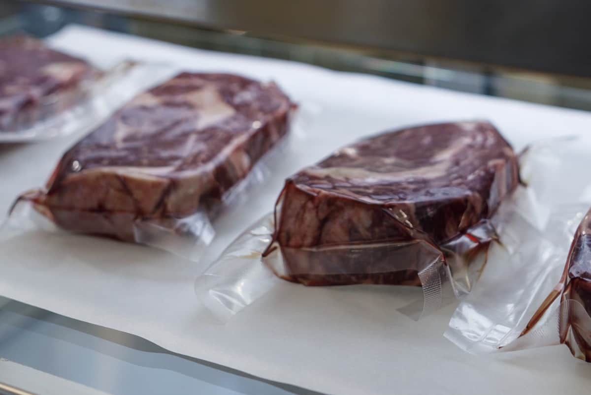 some raw, plastic wrapped steaks in a fridge