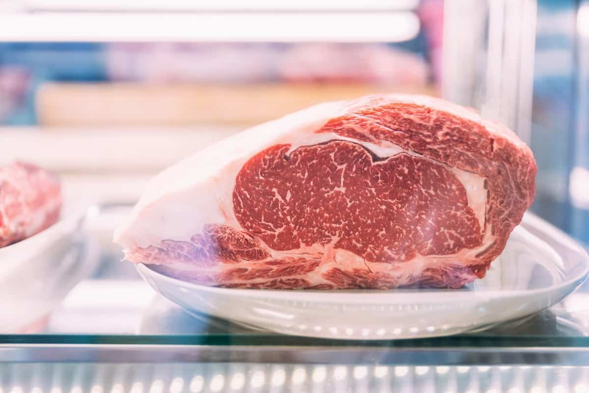 A thawed steak joint, on a white plate, in a refrigera.