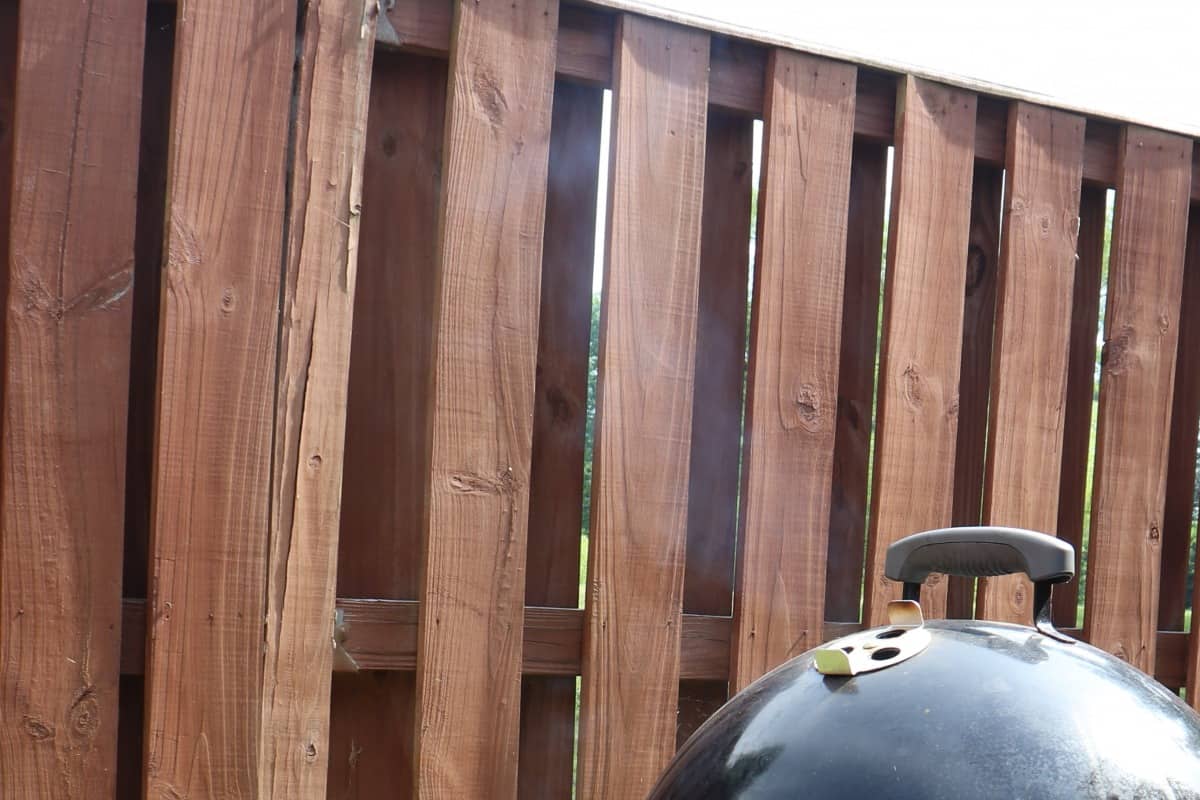 thin blue smoke from a smoker, against a dark wooden fence backgro.