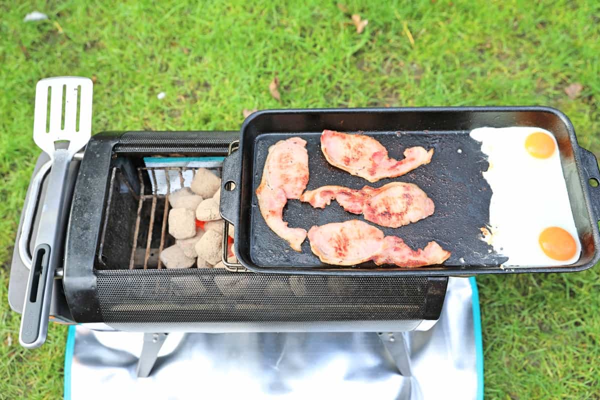 bacon and eggs being grilled on the Biolite Firepit+ griddle attachment
