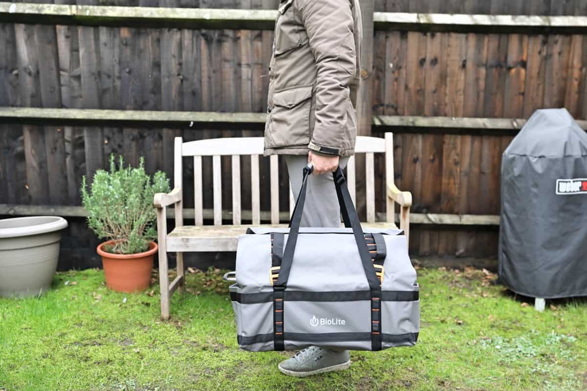 The BioLite firepit+ inside of the carry bag, being held up by a man in a garden.