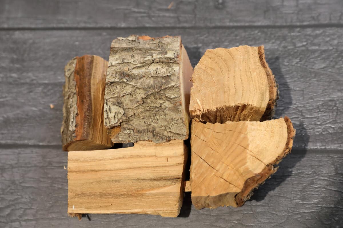 Five chunks of peach smoking wood on a dark wooden table.