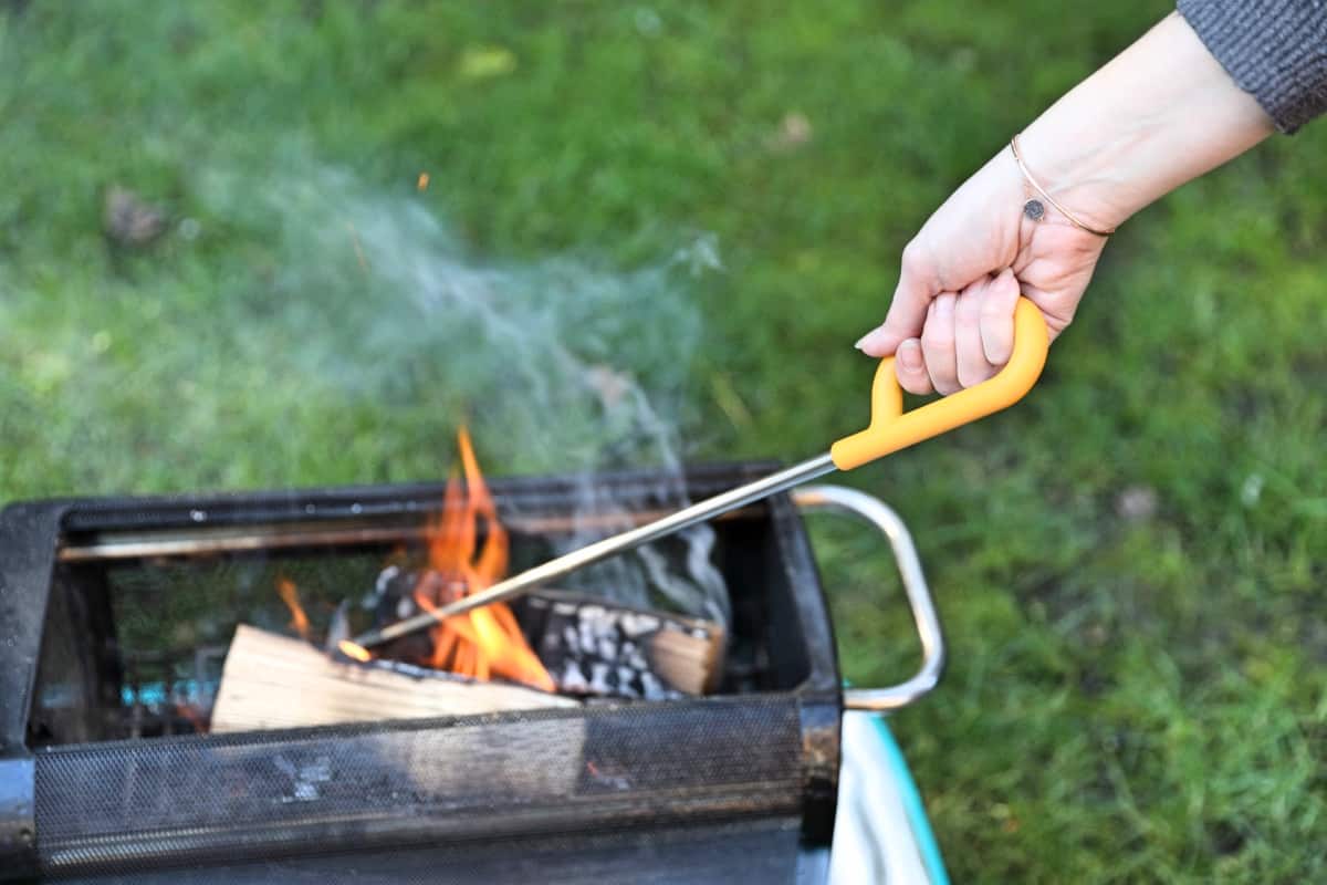 Biolite firepit poker in a womans hand, being used to poke a f.