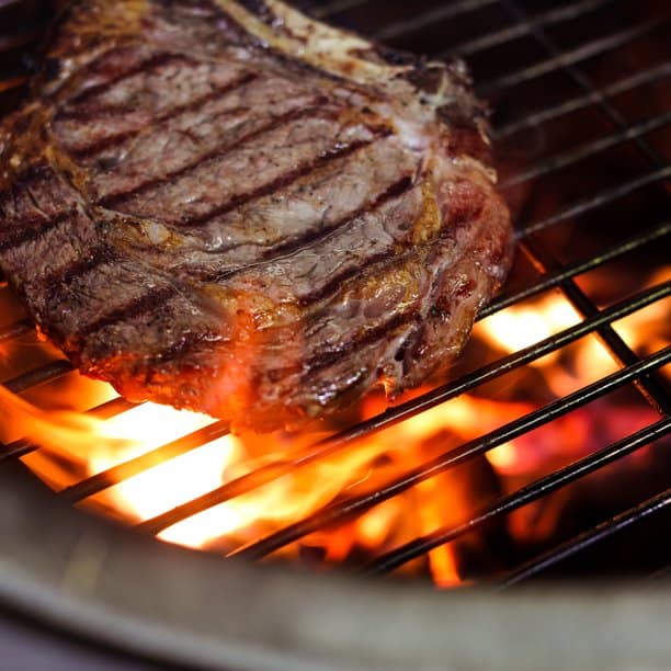 A steak with sear marks being grilled over flaming Royal Oak charcoal briquettes