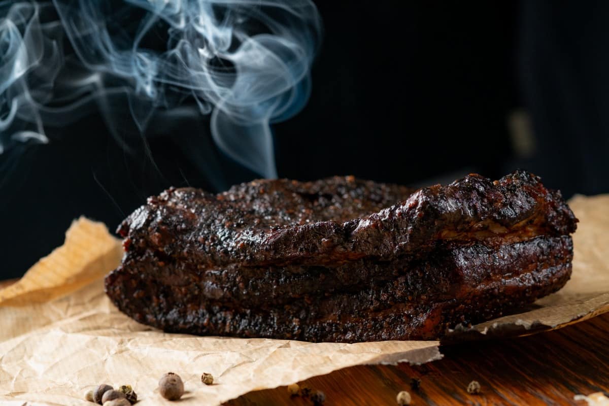 smoked beef brisket on pink butcher paper, a wisp of smoke rising in the backgro.