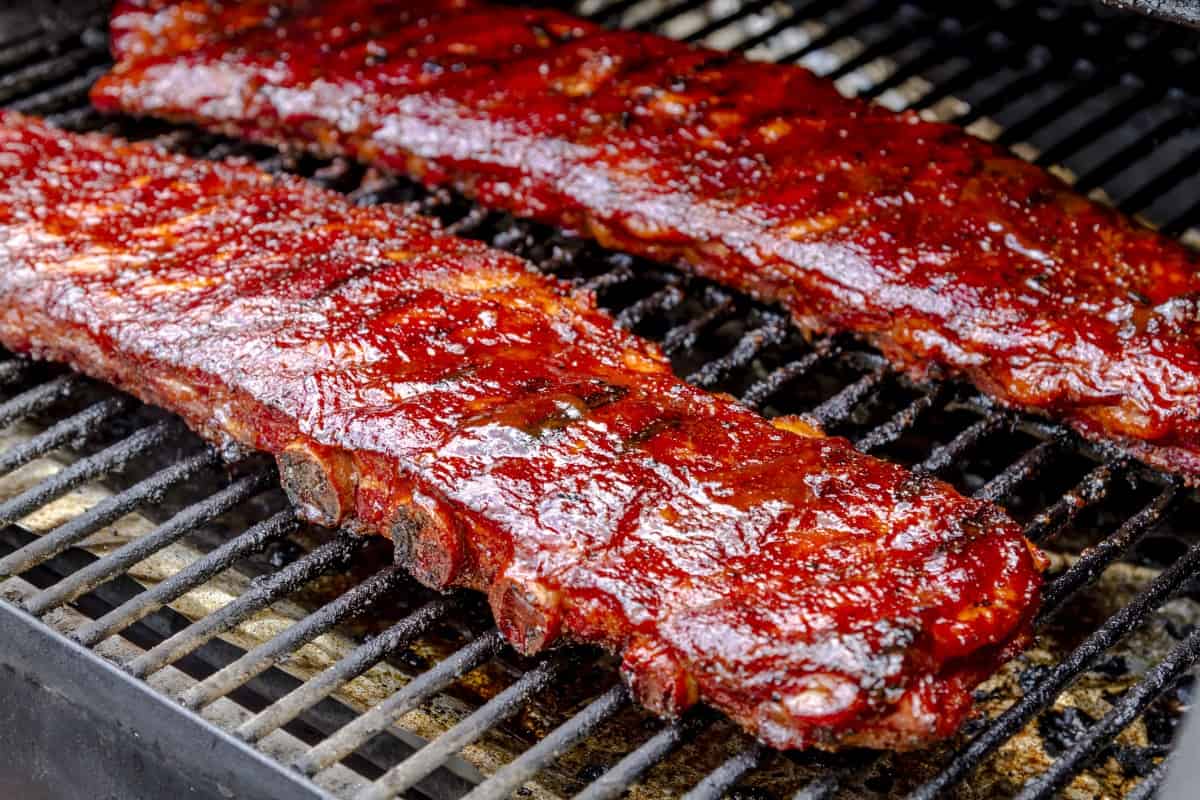 Two racks of pork ribs slathered in sauce, on the grate of a smoker.