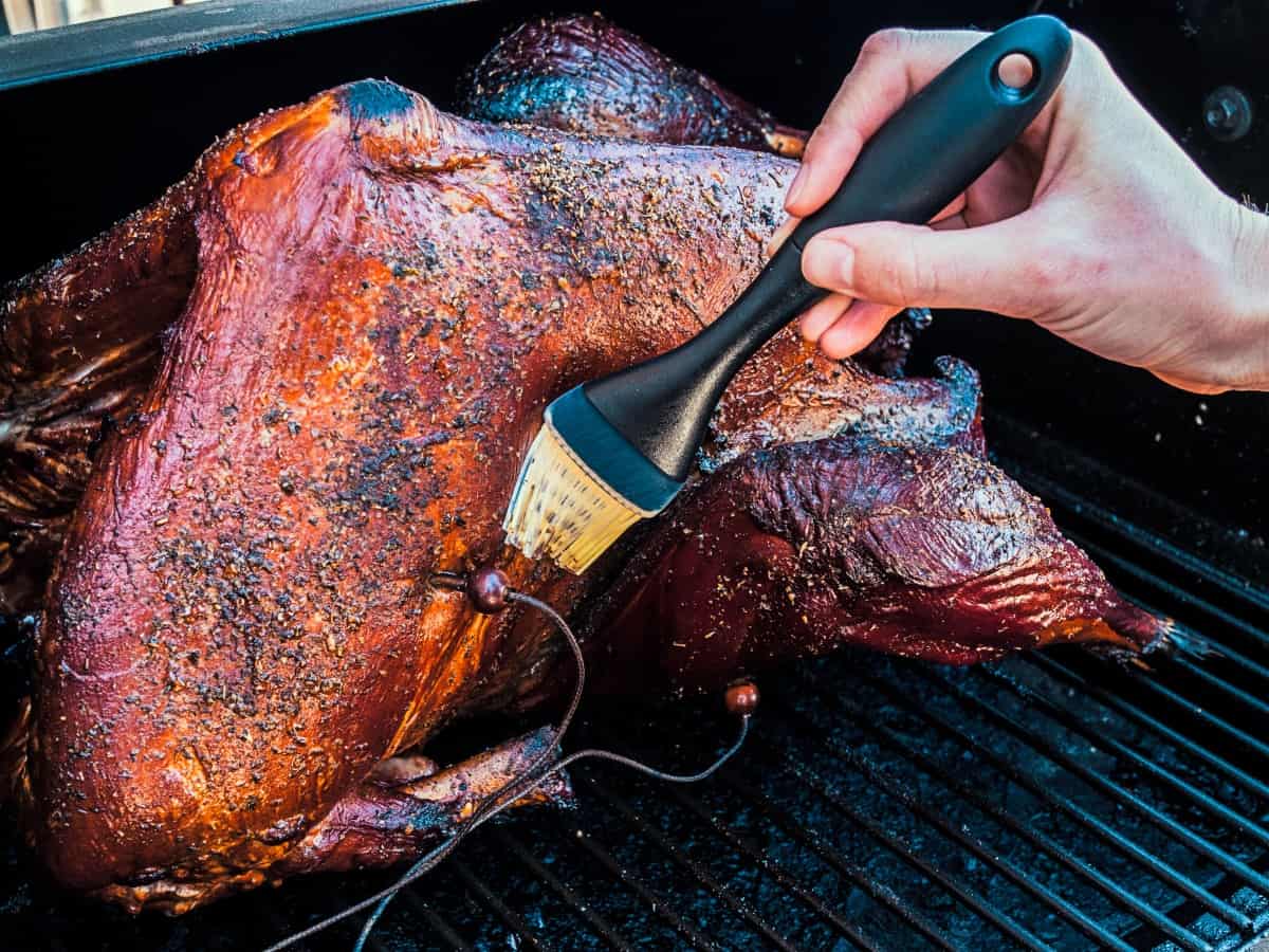 smoked turkey on the grill, being basted with a light colored bristle bru.