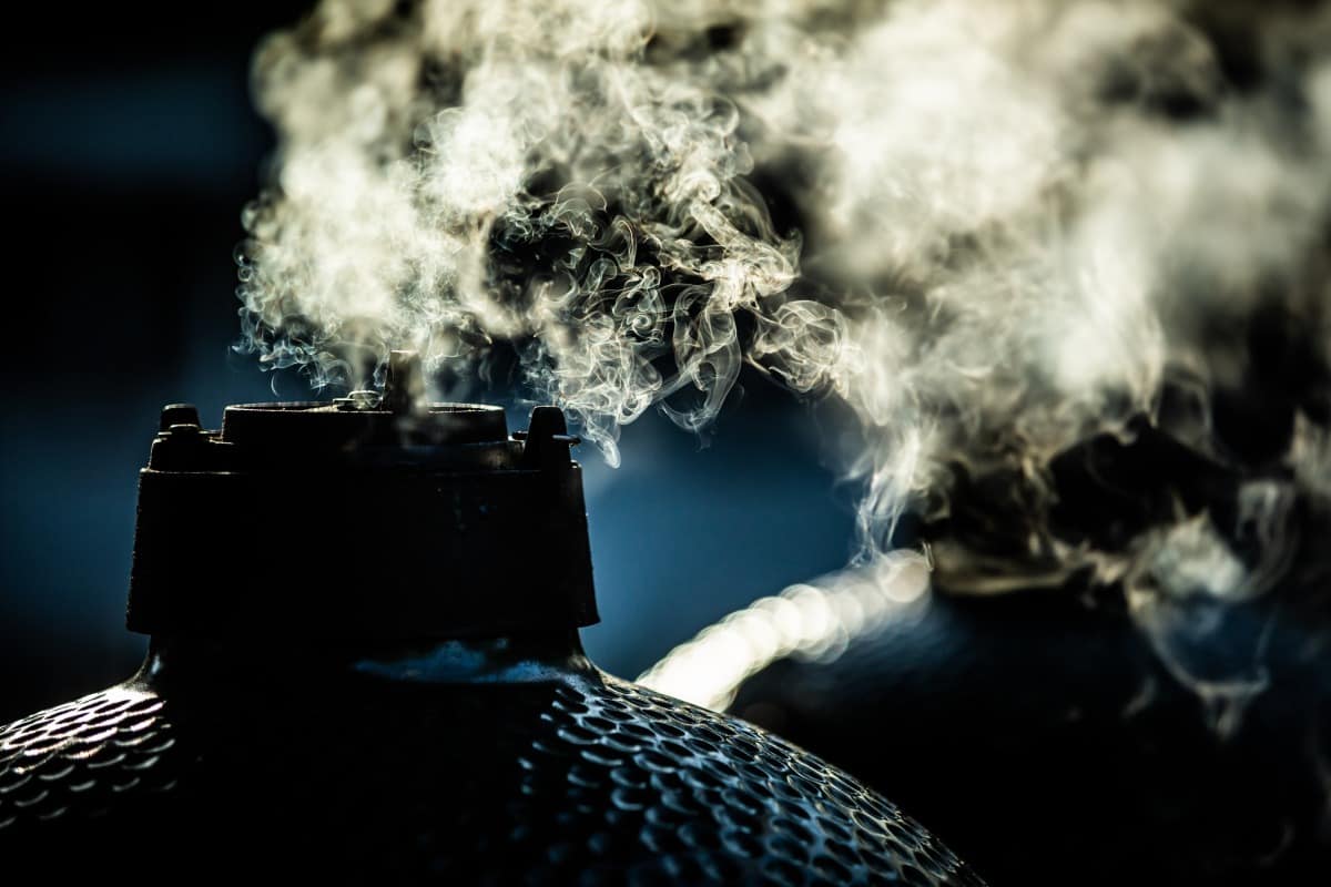Smoke coming out the top of a big green egg smoker, silhouetted on a bright sunny morning.