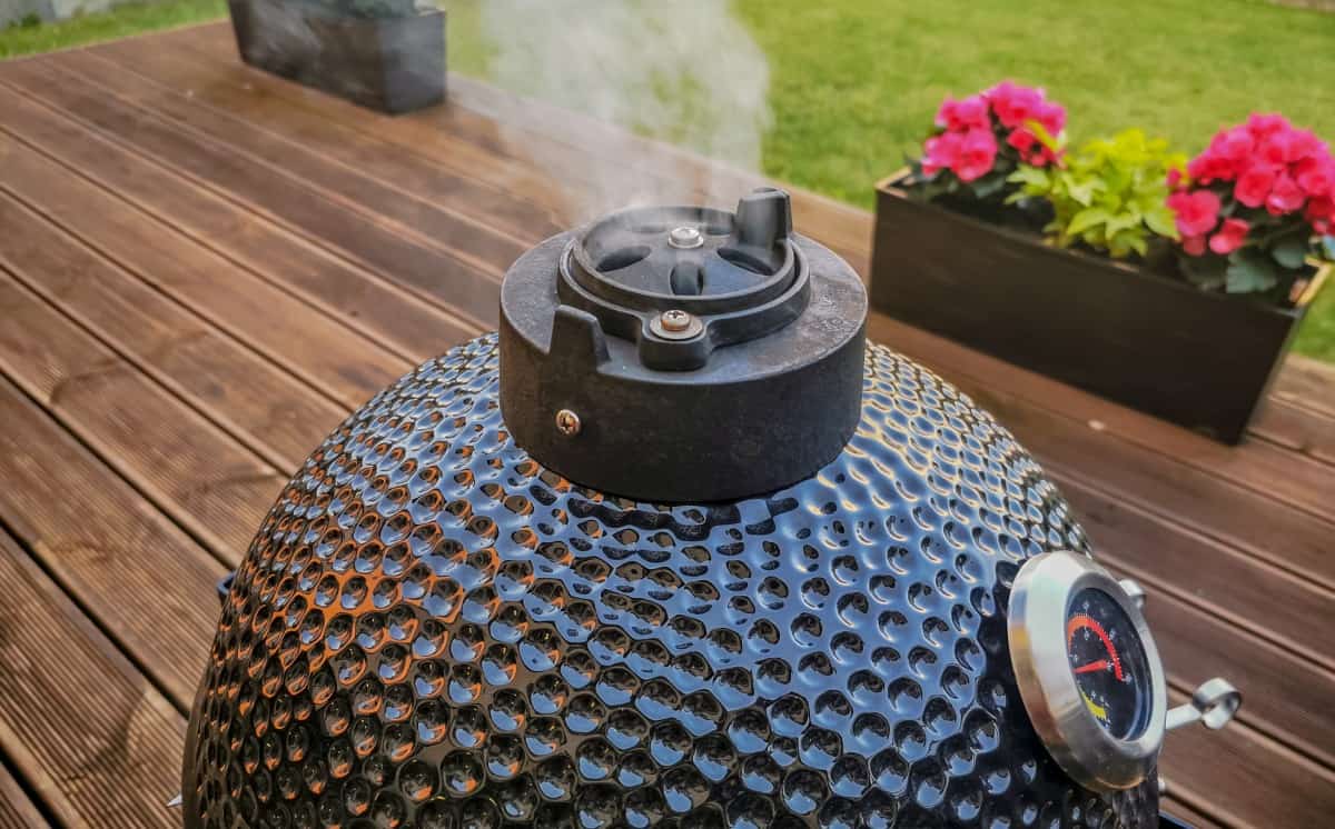 Smoke coming out of the top vent of a black ceramic kamado smo.