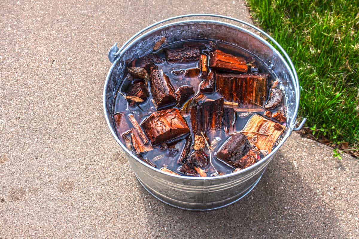 A bucket of water being used to soak smoking wood chunks.