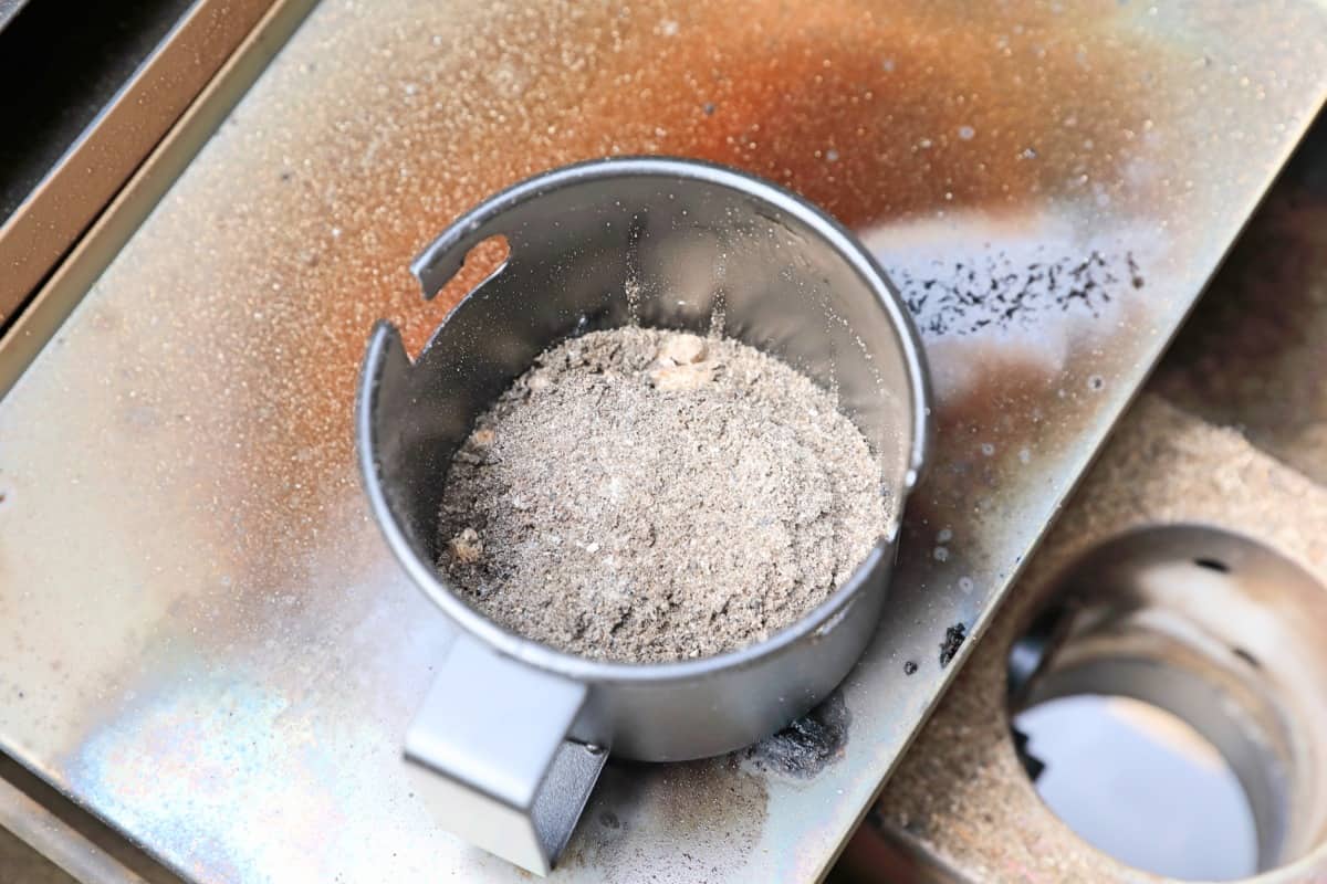 A Camp Chef Woodwind ash collection cup half full of ash, standing on the heat diffuser.