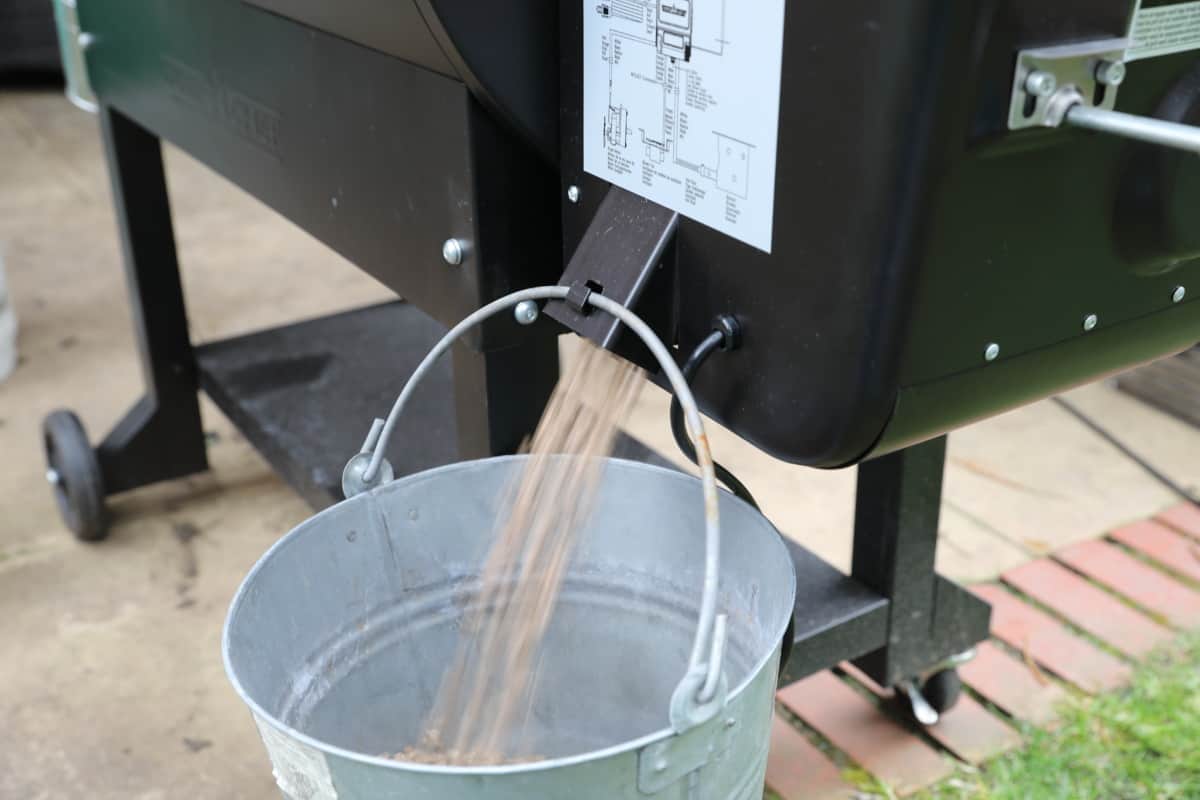 Emptying the hopper of a pellet grill into a silver, galvanized bucket