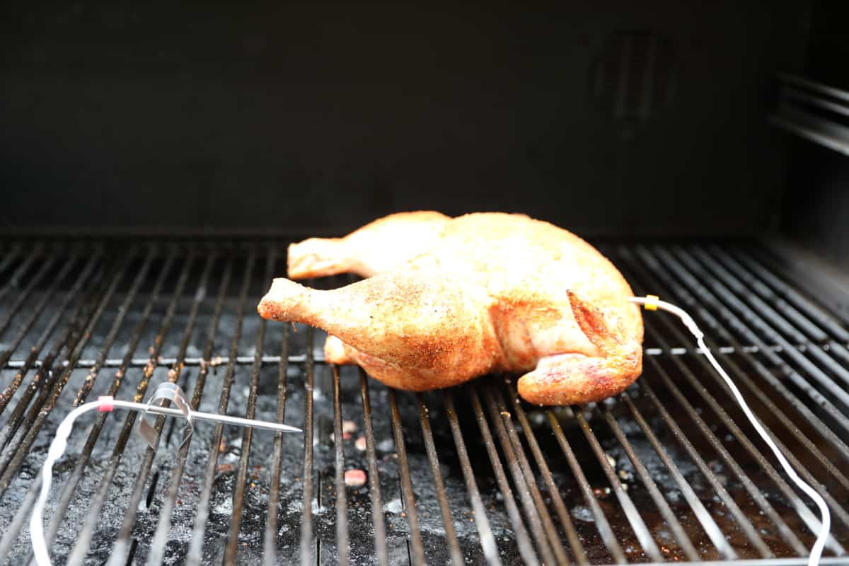 A whole chicken on a pellet grill, with a food probe inserted, and a second probe measuring the grill temp.