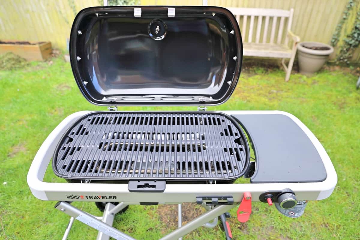 Close up of Weber Traveler BBQ with lid open, showing grates and side table.