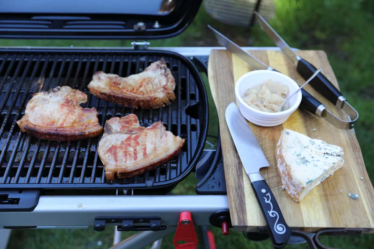 Pork chops on the Weber Traveler gas grill, with apple sauce and stilton on a cutting board