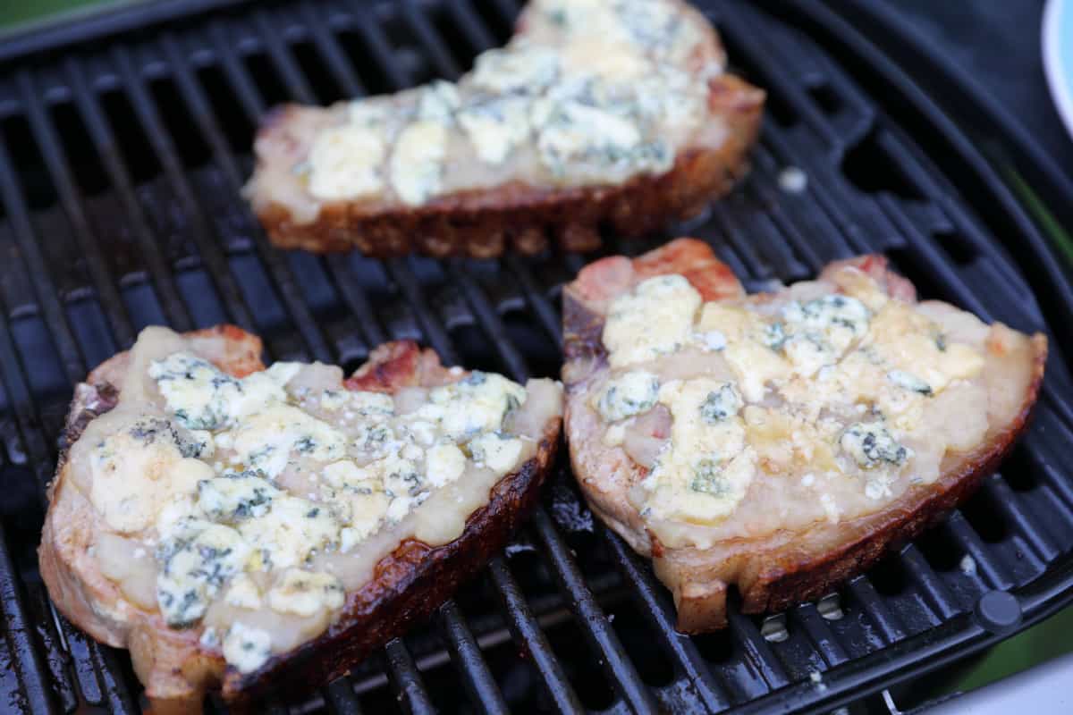 Pork chops with apple sauce and stilton on top, sitting on the grate of a Weber Traveler gas grill