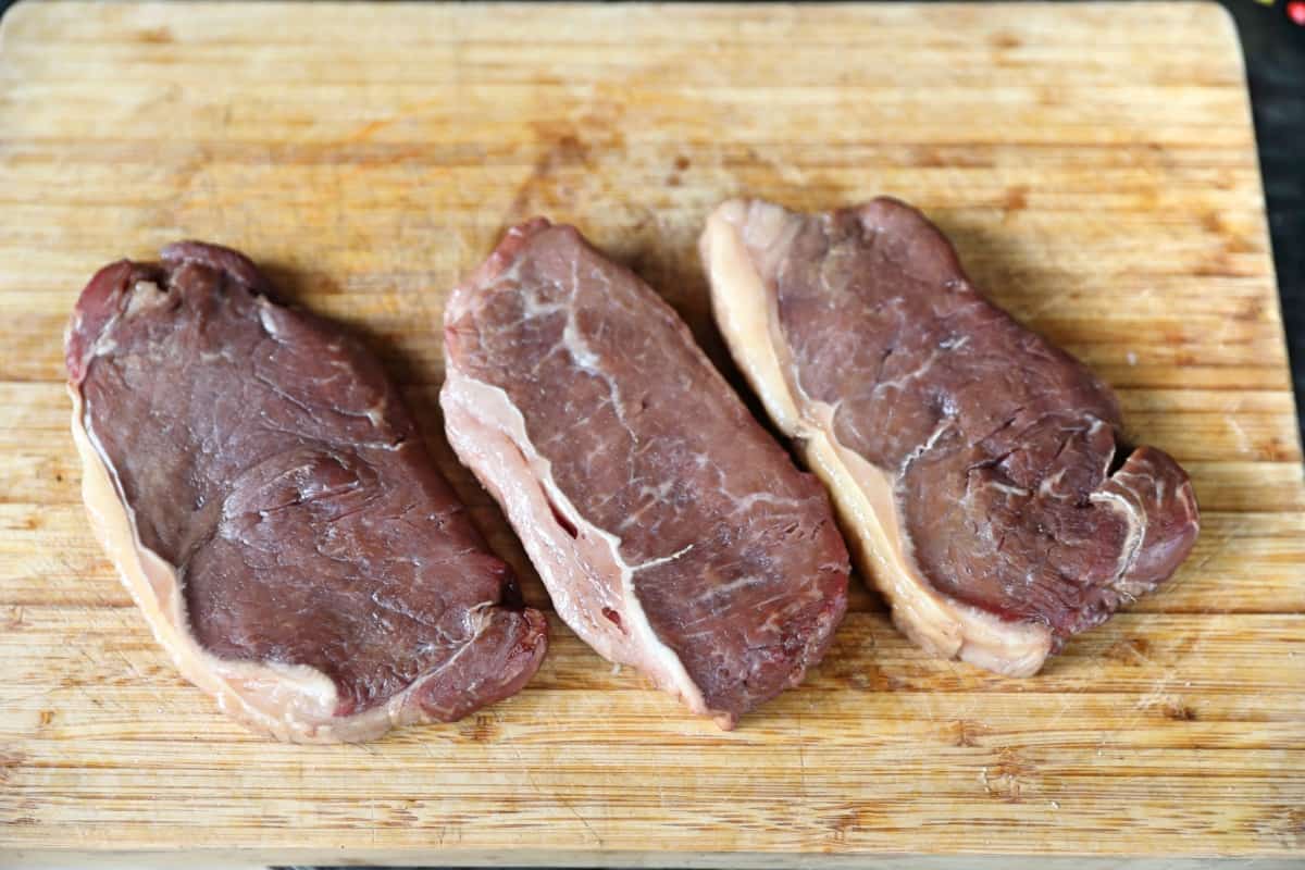 3 smoked steaks on a wooden chopping board.