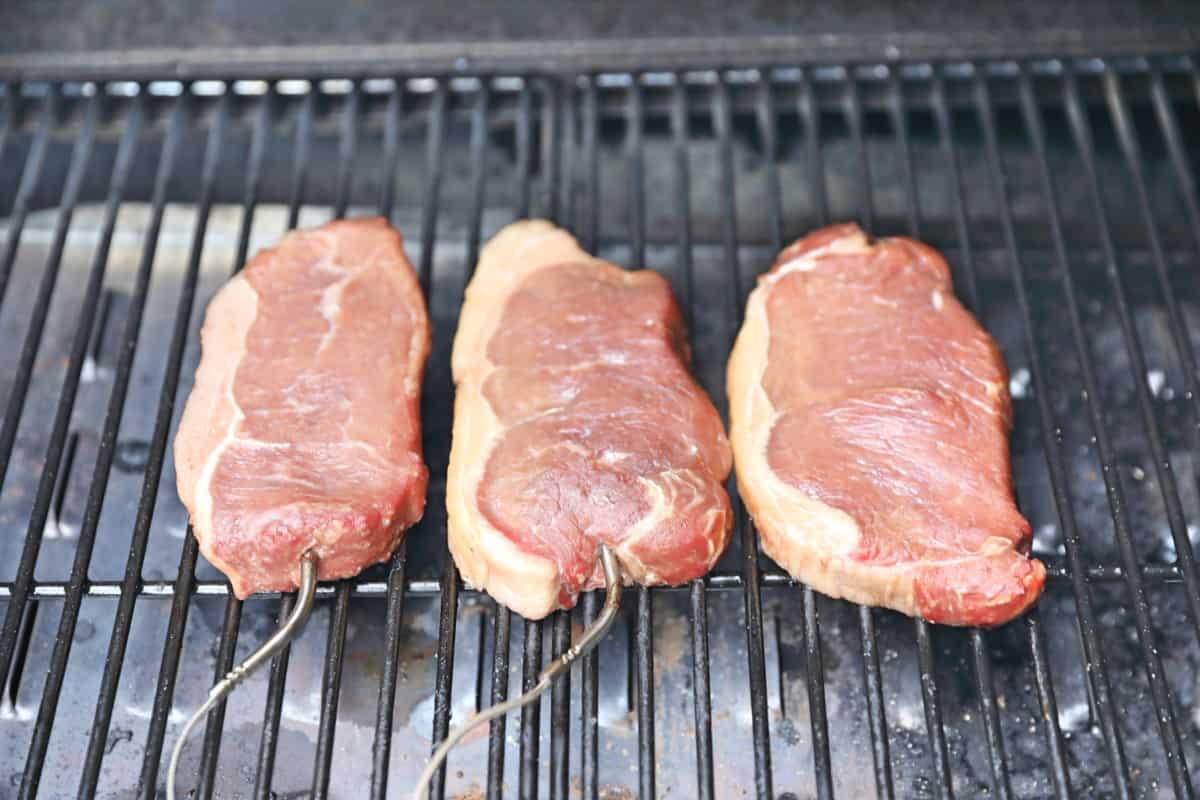 3 steaks on grates, being smoked in a pellet smoker.