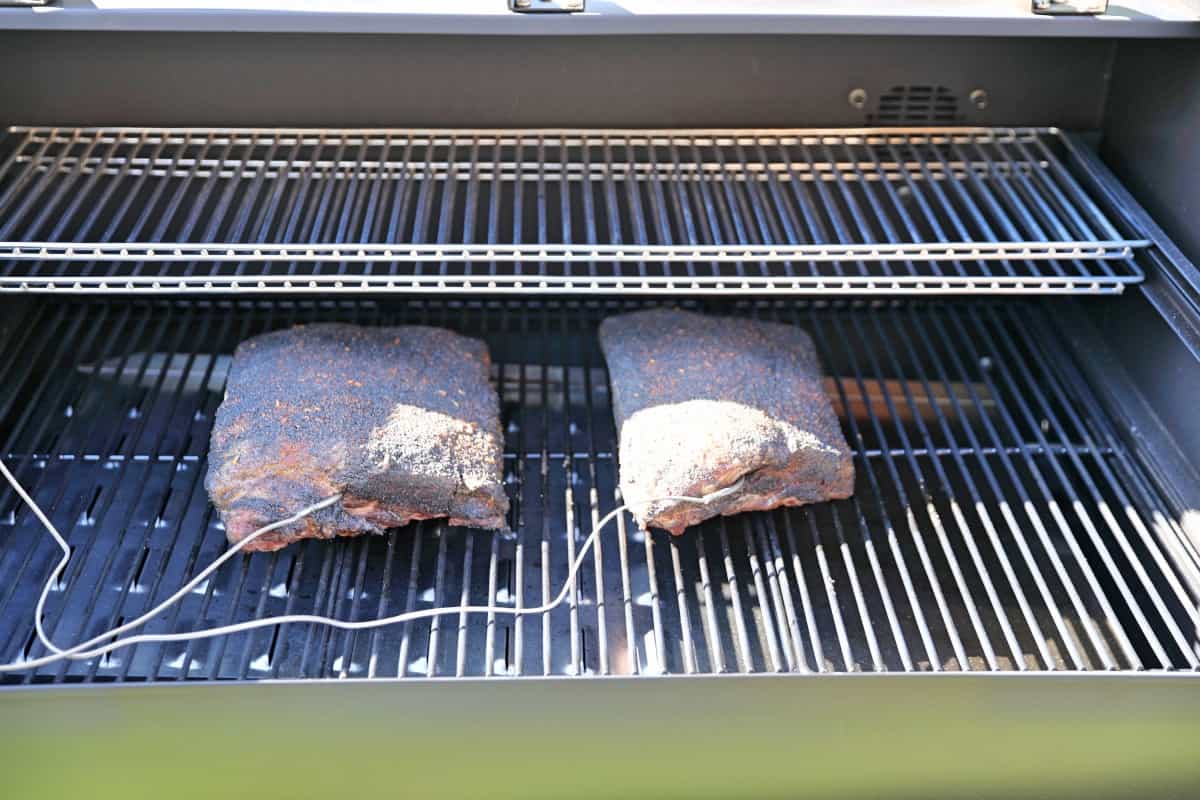 Two racks of beef ribs smoking in a Camp Chef Woodwind pellet grill.