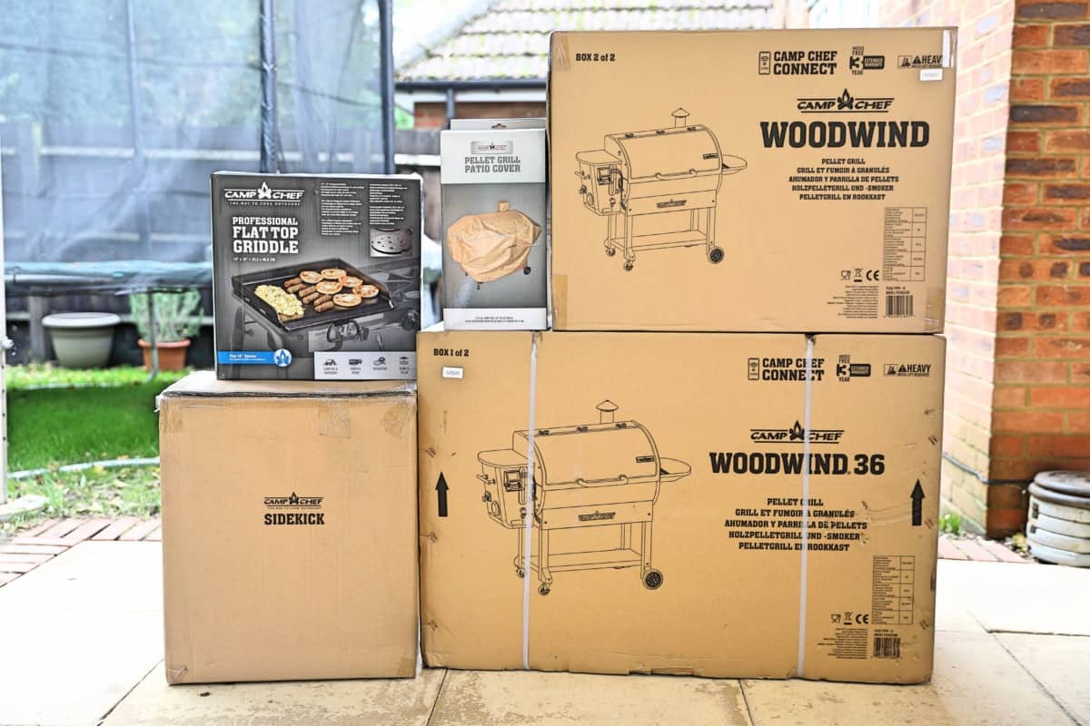 A pile of 5 boxes, containing the Camp Chef Woodwind Wi-Fi smoker, griddle, and a cover.