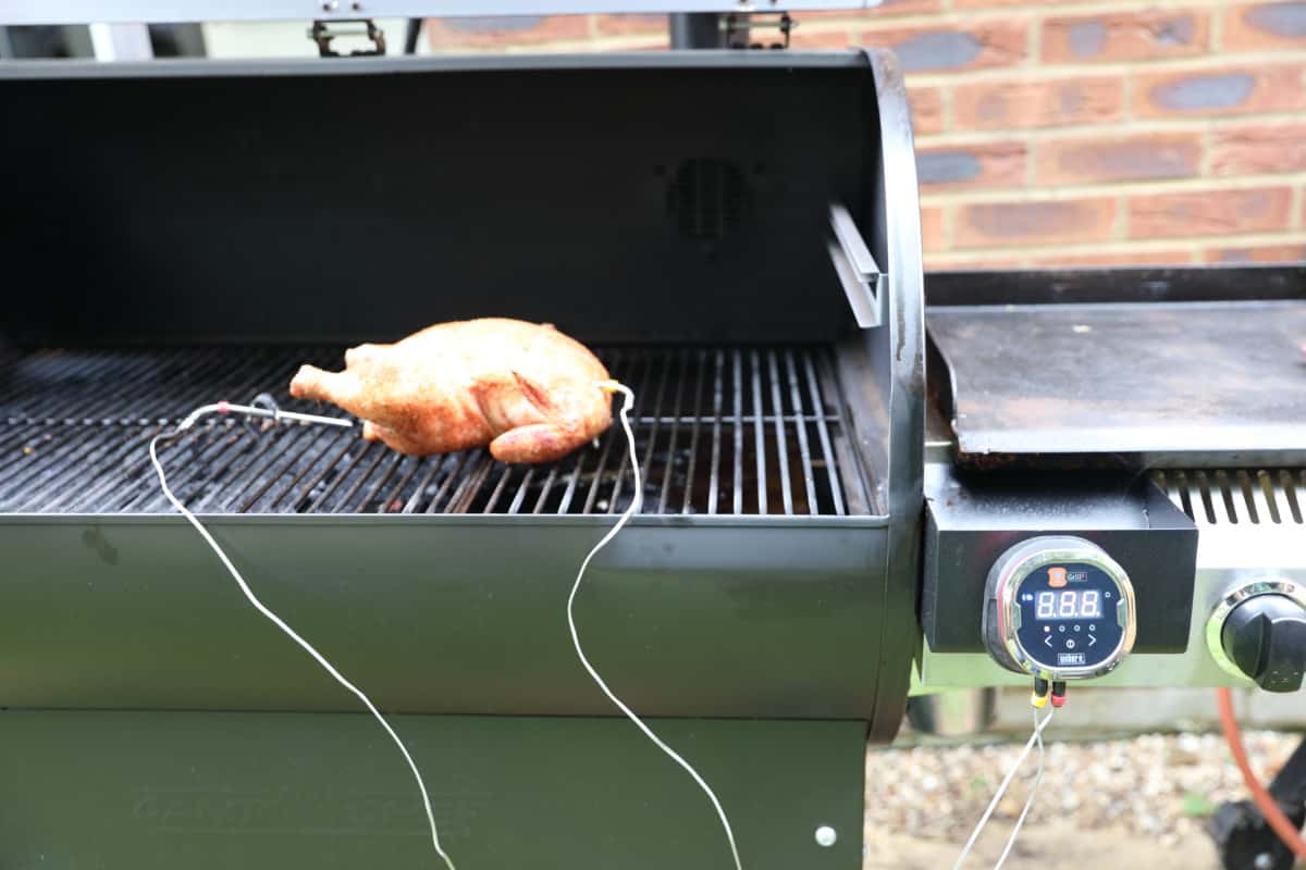 weber igrill 2 in use, magnetically stuck to the side table of a pellet grill that is smoking a chicken.