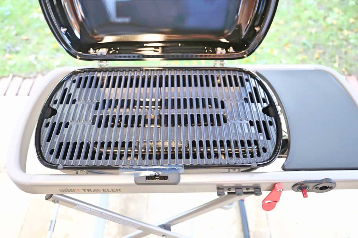 Close up of Weber traveler BBQ with lid open, showing grates, burner, and side ta.