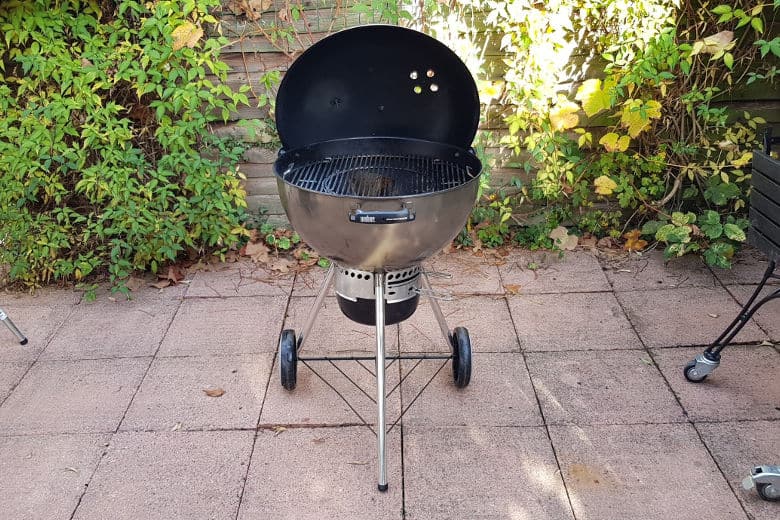 Weber Master Touch charcoal grill on a paved patio, with the lid open and in the hol.