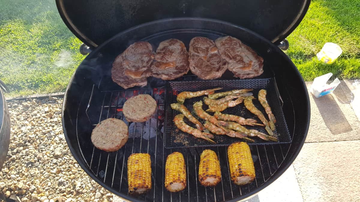 Weber Master Touch with steaks, prawns, and corn being gril.