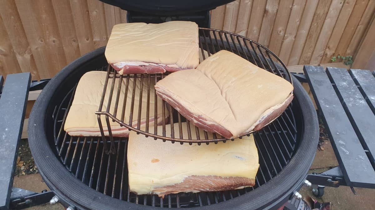 Five pork bellies being smoked inside a Kamado Joe Big Joe III for making bacon.