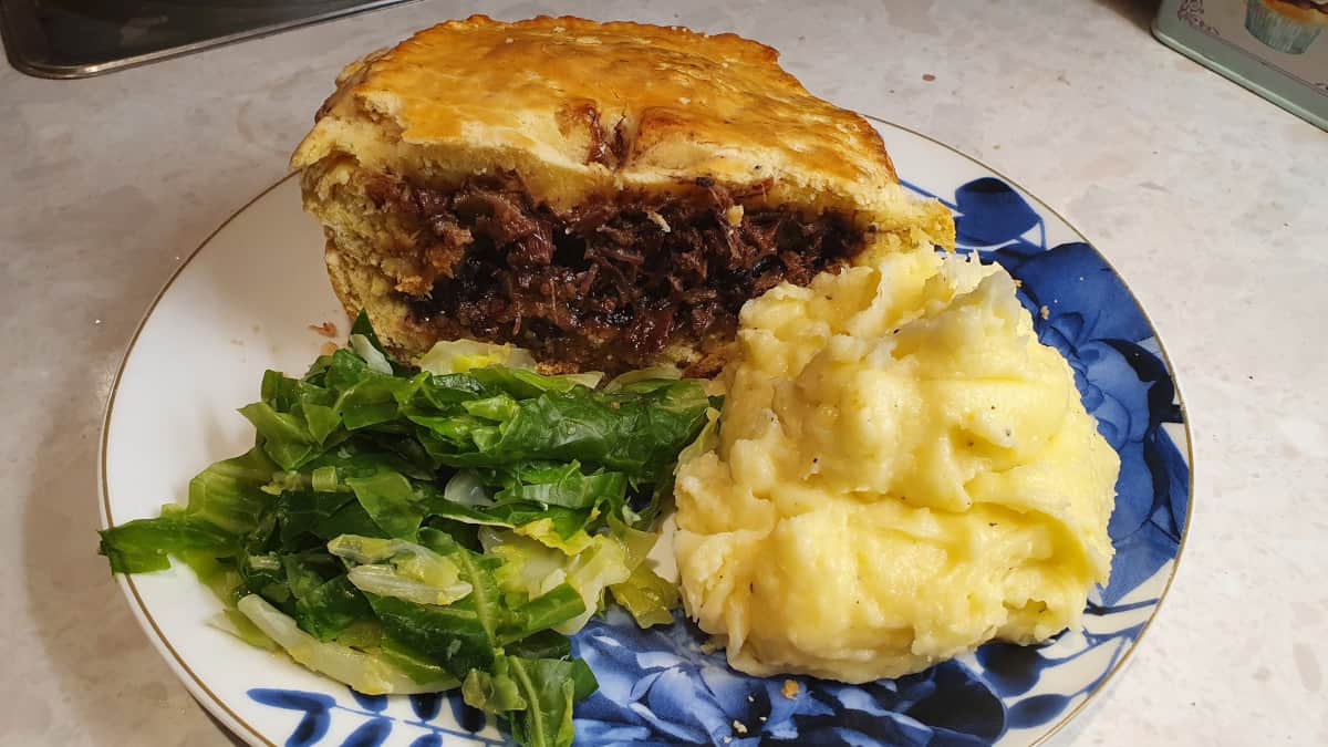 A plate with a pie, mash, and greens