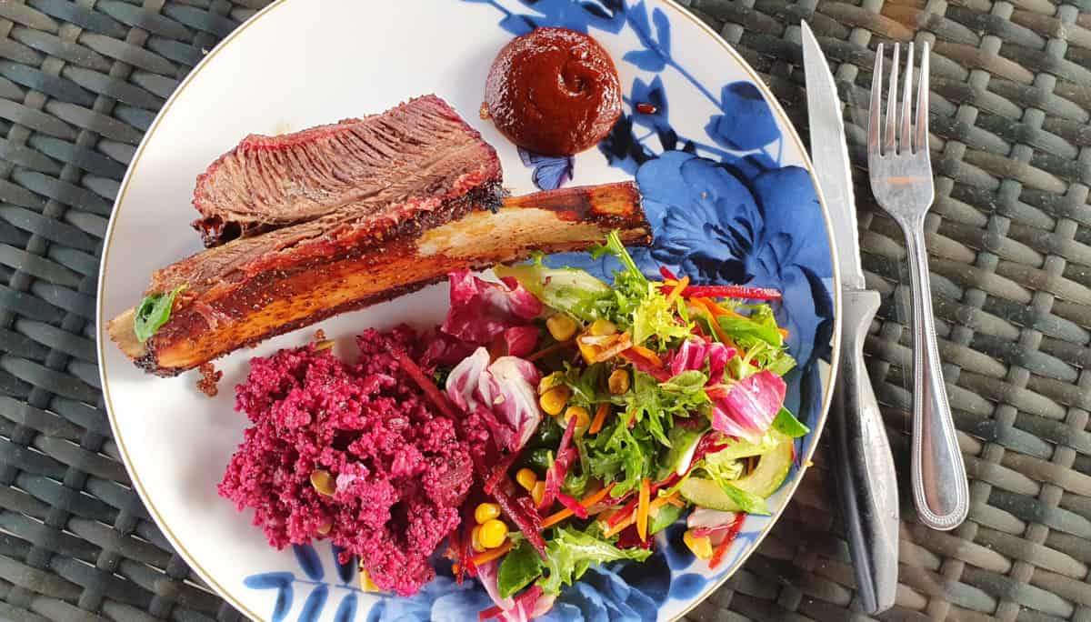 Smoked beef rib, salad and sauce on a floral plate.