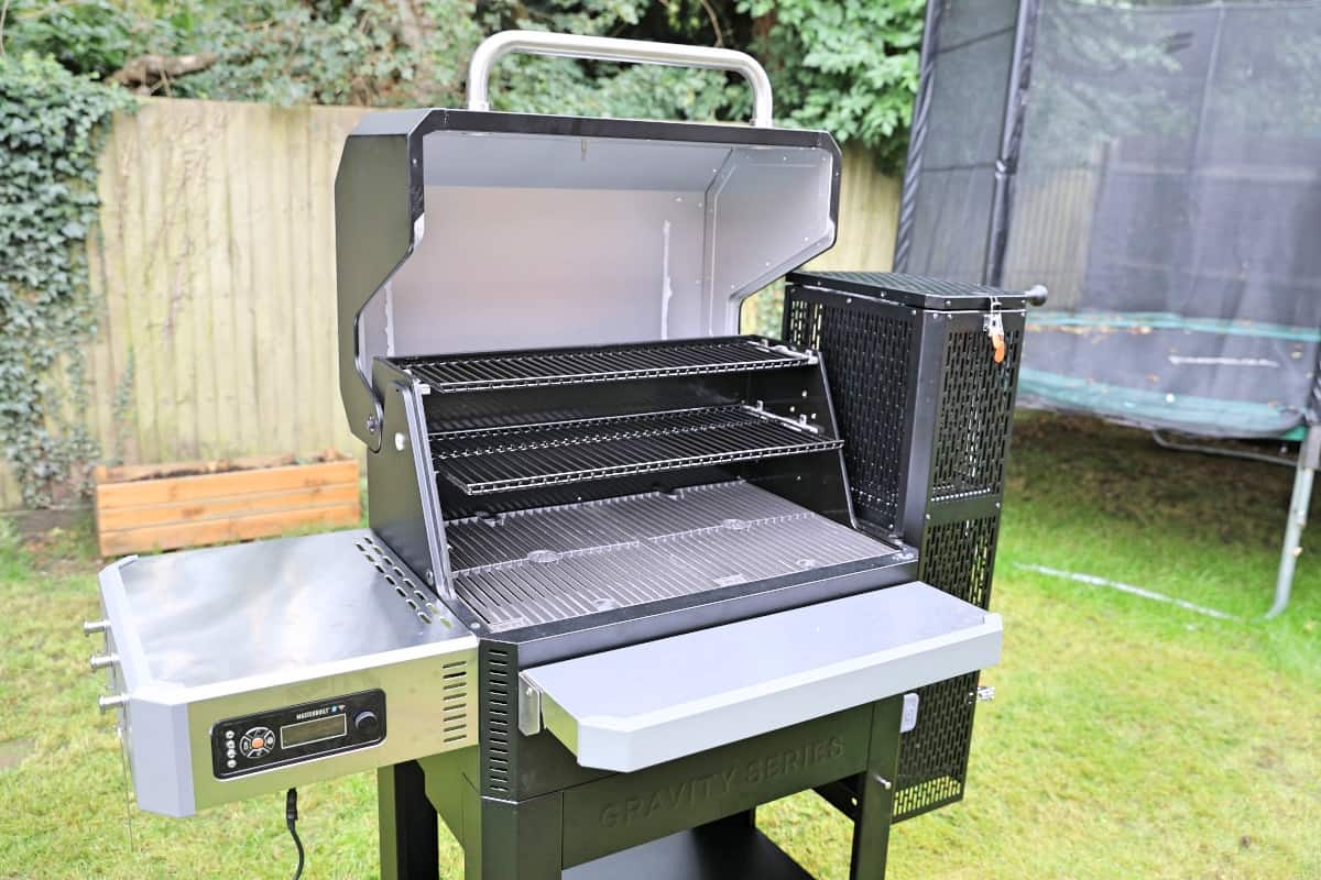 Masterbuilt gravity series smoker with its lid open, stood on a grass l.