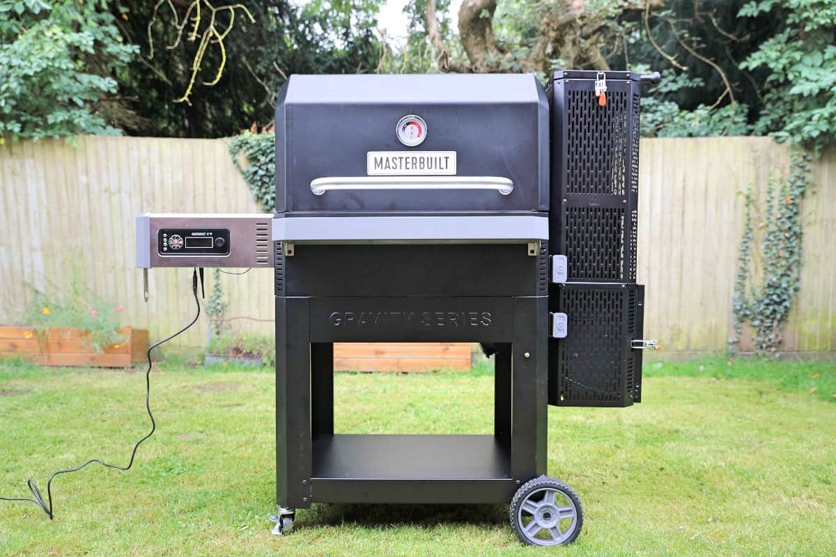 A Masterbuilt gravity series 1050 smoker and grill on a grass lawn.