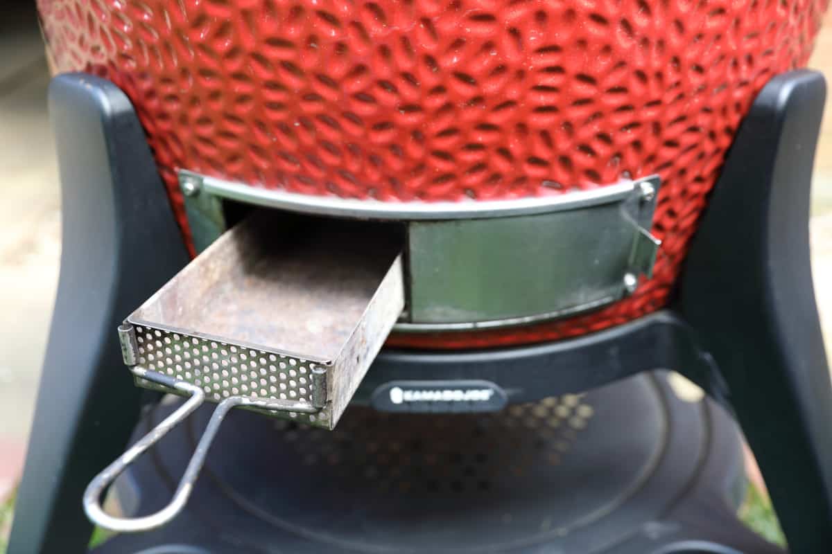 The removable ash tray being pulled out from the lower vent of the Kamado Joe smoker.