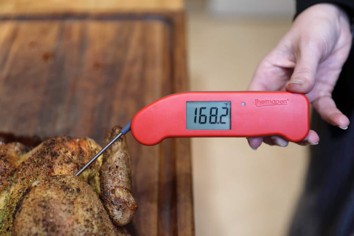 Thermapen one in a woman's hand, inserted into chicken on a cutting board, displaying 168..2 degrees Fahrenheit