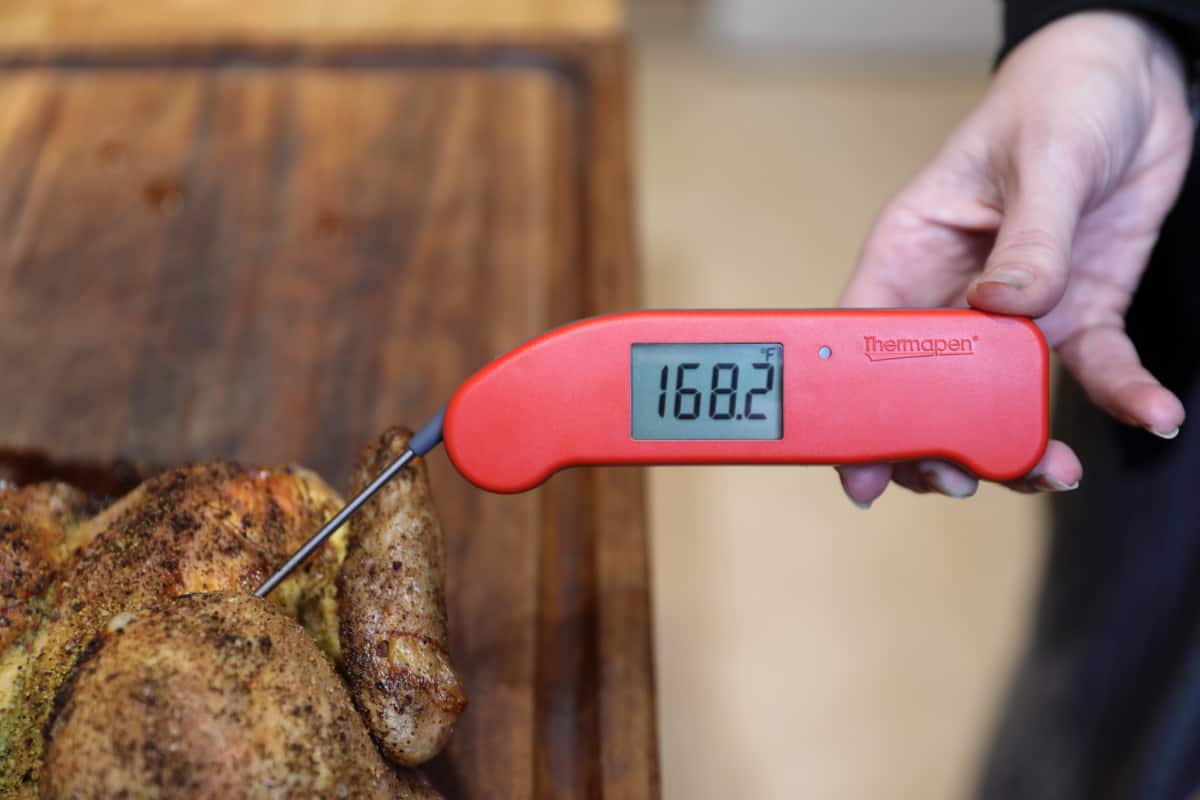 Thermapen one in a woman's hand, inserted into chicken on a cutting board, displaying 168.2 degrees Fahrenh.