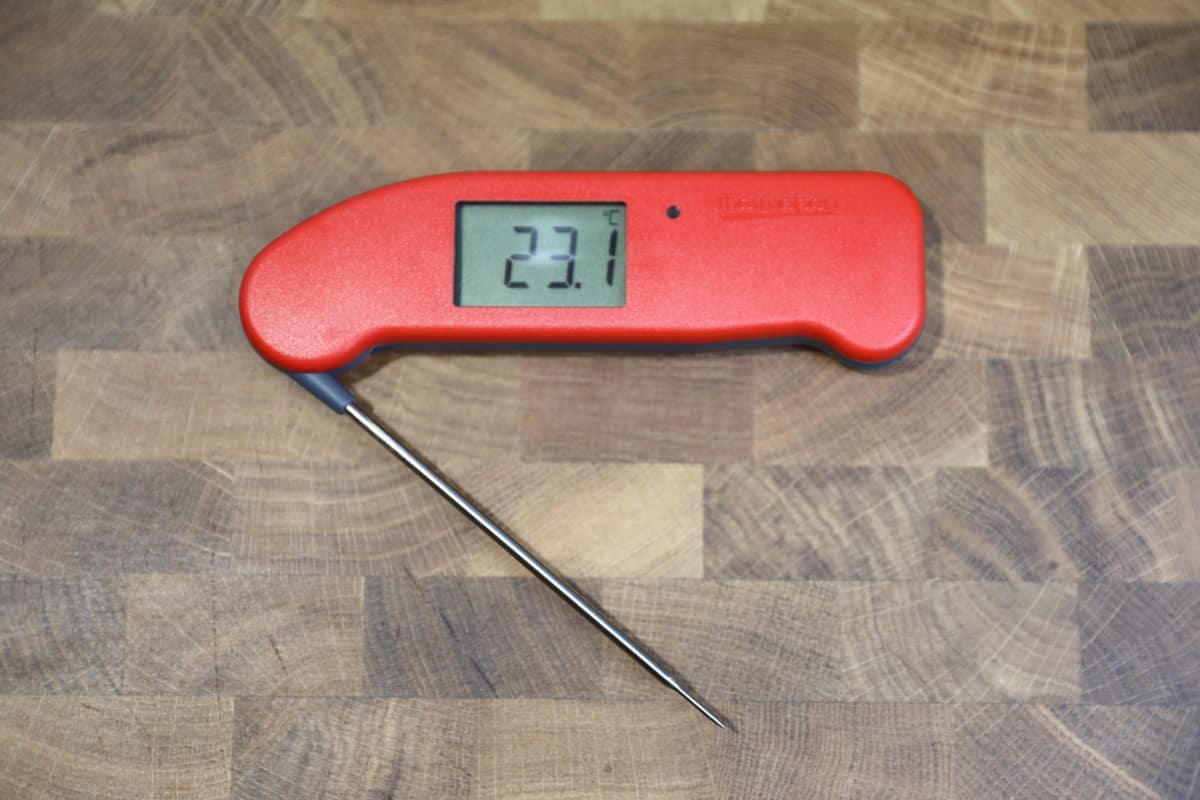 Thermapen one on a wooden chopping board, opened and displaying 23.1 degrees Cels.
