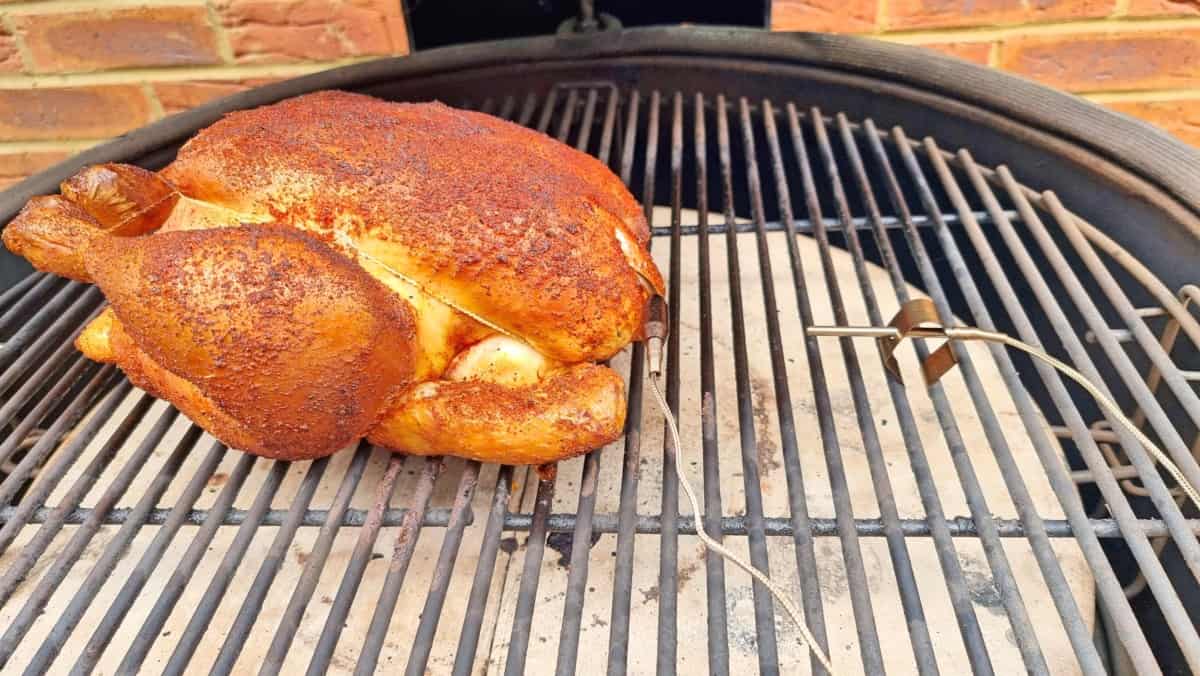 A smoked chicken in a Kamado Joe, with a food probe inserted, and an ambient temperature probe inserted between grill gra.