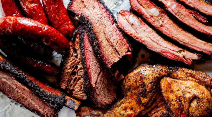 Close up of a large bbq platter with pork ribs, brisket, chicken, and sausages.