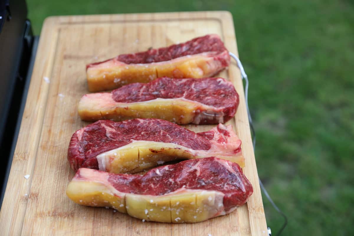 Four ex dairy cow sirloin steaks on a wooden cutting bo.