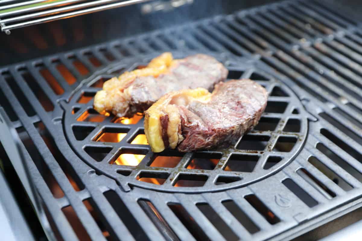 Two sirloin steaks on a gas grill, with flames coming up from the flavorizer ba.