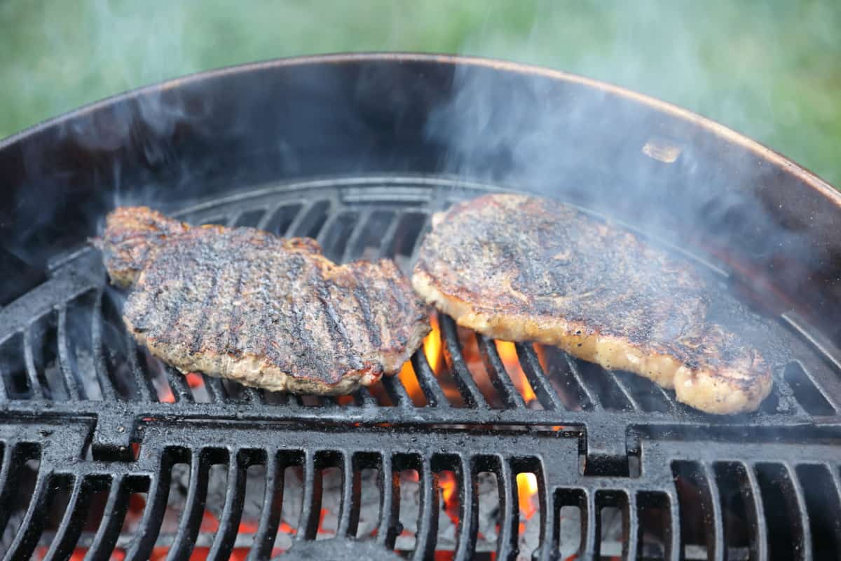 Two steaks being grilled on a Napoleon PRO22K-LEG-2 charcoal grill