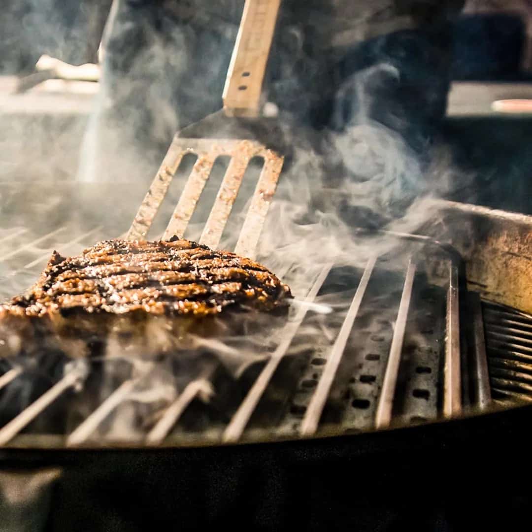 A steak being seared on a round grill with Grill Grates in.
