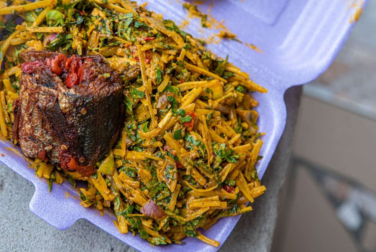 A purply take away carton full of abacha and some type of meat stuffed with red pepp.