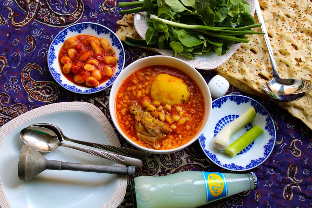 A bowl of Abgoosht, next to bowls of other finger food and some type of flat br.