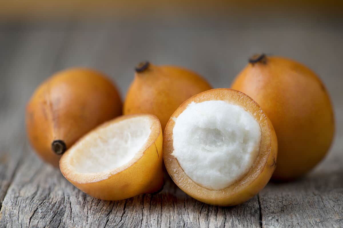 A halved achacha fruit, showing the soft white insides, sitting in front of 3 whole achacha beh.